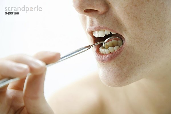 Frau überprüft ihre Zähne mit einem Mundspiegel