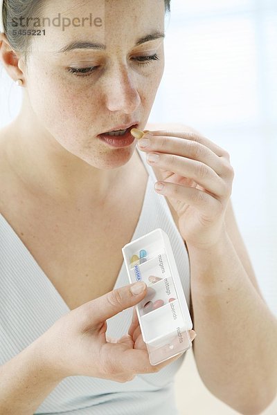 Frau nimmt eine Tablette aus einer Pillendose ein