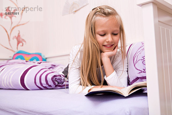Mädchen liest in einem Buch  liegt im Bett