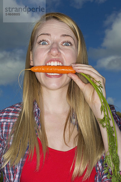 Frau beißt Karotte im Freien
