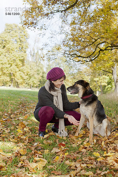 Lächelnde Frau streichelt Hund im Park