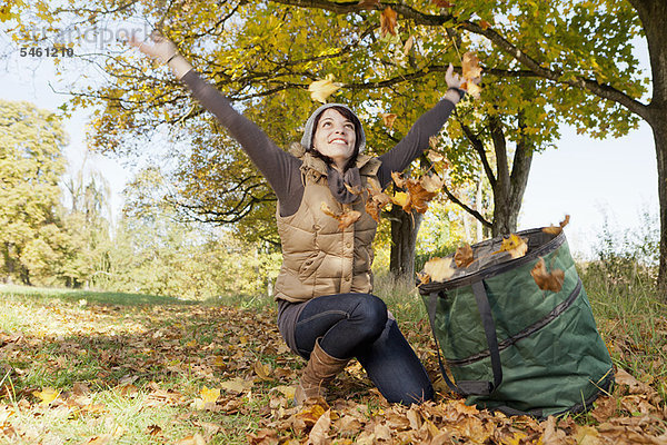 Frau spielt mit Herbstblättern im Park