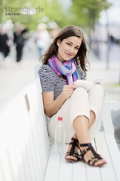 Portrait of young Woman reading Book on Bank