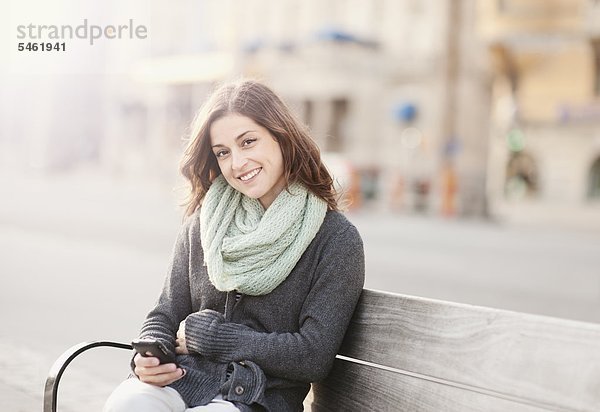 Portrait of young Woman sitting on Bench mit Telefon