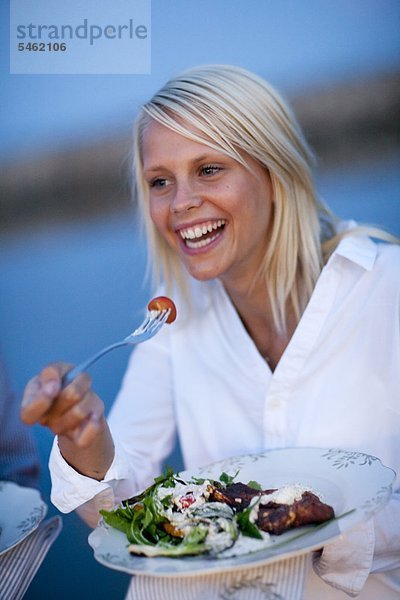 Junge Frau mit Essen an der K??ste  lächelnd