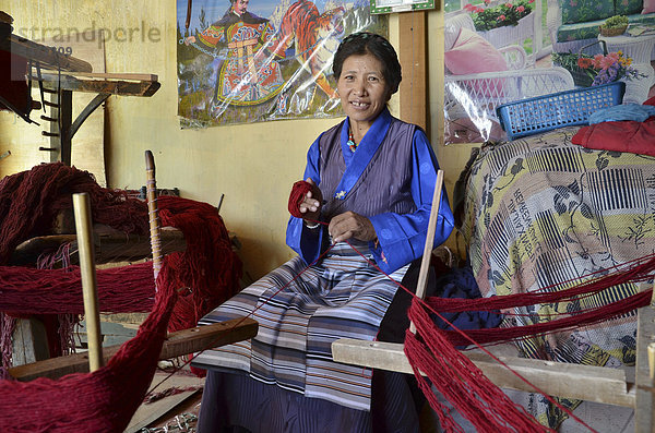 Tibetische Frau in Tracht beim Verarbeiten von roter Yakwolle  tibetisches Handwerk  Yakwollweberin  Tibet  China  Asien