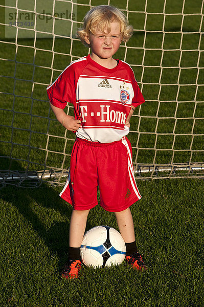 Fünfjähriger Junge in FC Bayern München Dress steht mit Fußball im Fußballtor