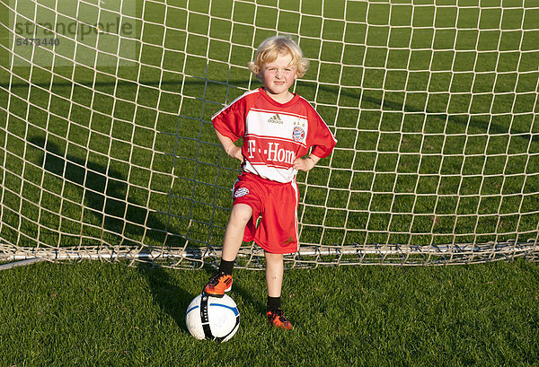 Fünfjähriger Junge in FC Bayern München Dress steht mit Fußball im Fußballtor
