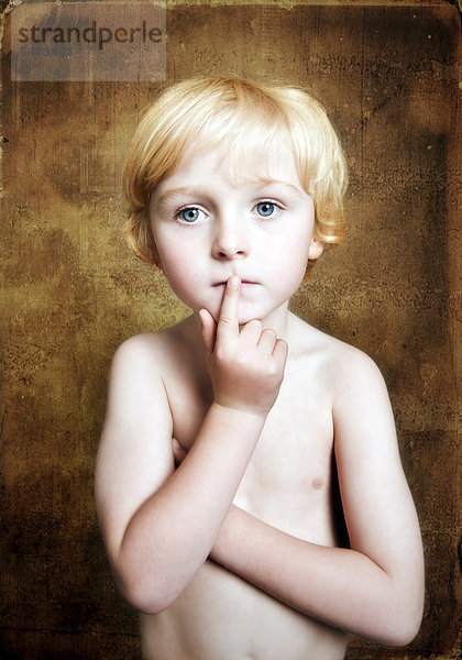 Fünfjähriger Junge mit freiem Oberkörper hält nachdenklich den Finger vor den Mund  Portrait