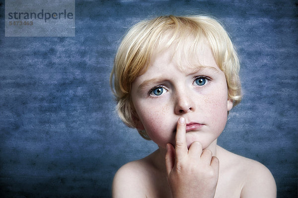 Fünfjähriger Junge hält nachdenklich den Finger vor den Mund  Portrait