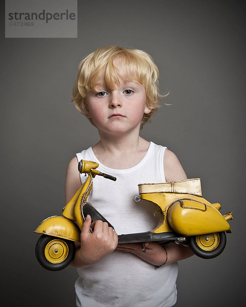 Fünfjähriger Junge hält Spielzeug-Vespa-Roller in der Hand  Geschenk  trauriger Blick