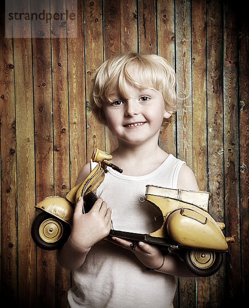 Fünfjähriger Junge hält Spielzeug-Vespa-Roller in der Hand  Freude über Geschenk
