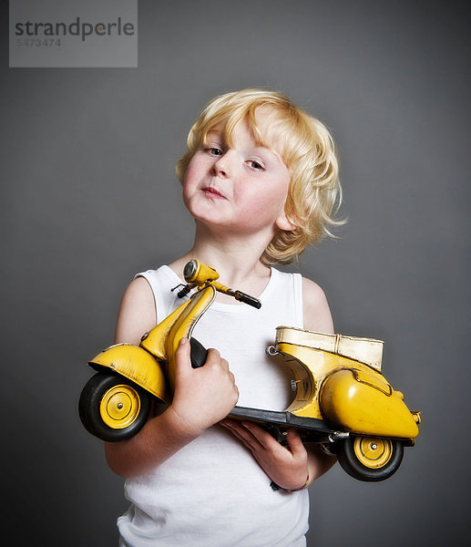 Fünfjähriger Junge hält Spielzeug-Vespa-Roller in der Hand  Freude über Geschenk