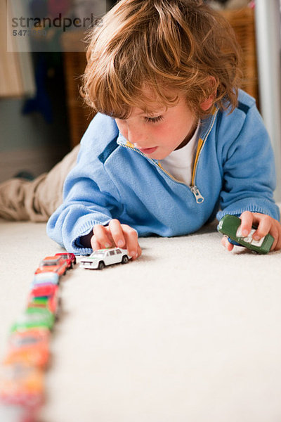Kleiner Junge  der Spielzeugautos in seinem Schlafzimmer anstellt.
