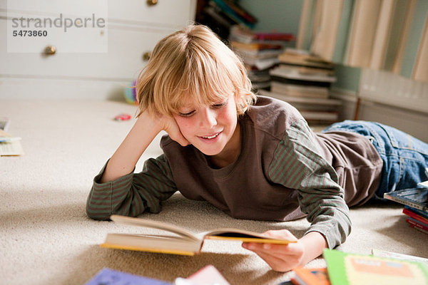 Kleiner Junge  der auf seiner Vorderseite liegt und ein Buch in seinem Schlafzimmer liest.
