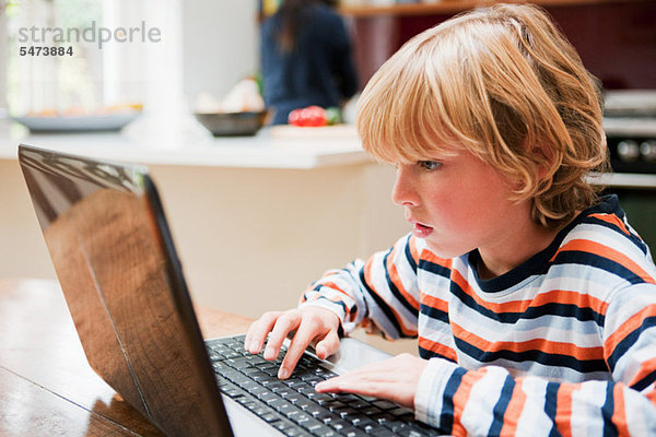 Junge schaut beim Tippen auf einen Laptop-Monitor