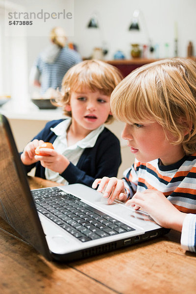 Kleiner Junge mit Laptop und seinem jüngeren Bruder mit Blick auf den Monitor