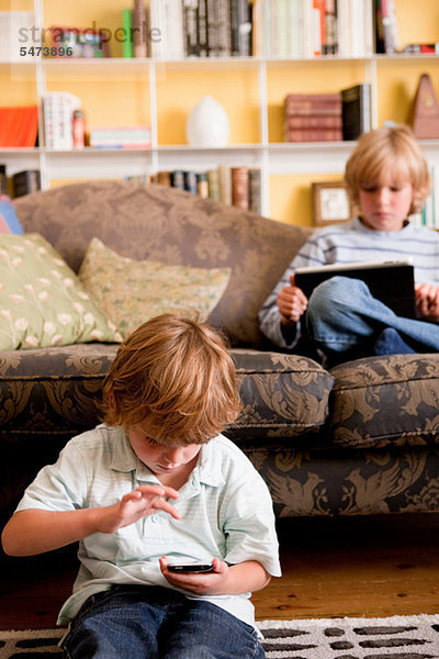 Zwei Jungen entspannen sich zu Hause mit einem digitalen Tablett und einem Smartphone.
