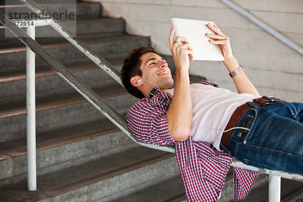 Junger Mann mit einen digitalen Tablet beim liegen auf einem Geländer