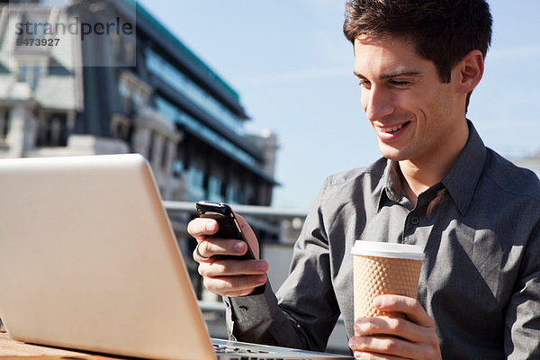 Junger Mann arbeiten im Freien mit seinen Laptop und Handy