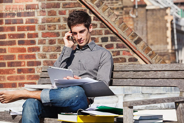 Junger Mann sitzt auf einer Bank mit digitalem Tablett und Handy