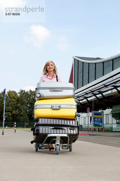 Mittlere erwachsene Frau schiebt Gepäckwagen zum Flughafen