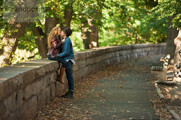 Junges Paar umarmt an der Wand im Park