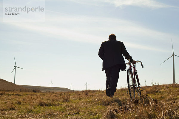 Man zieht Fahrrad bergauf in Richtung windfarm