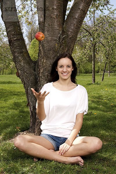 Junge Frau sitzt mit einem Apfel auf einer Wiese