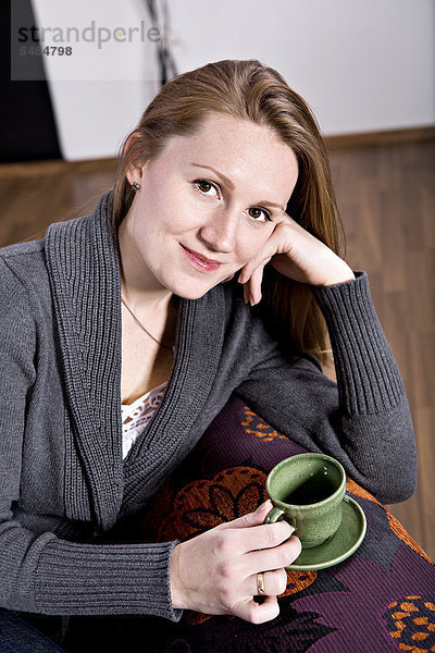 Eine junge Frau trinkt Kaffee im Wohnzimmer