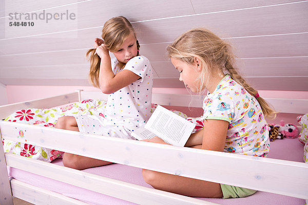 Zwei Schwestern sitzen im Bett und lesen ein Buch