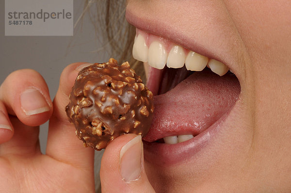Junge Frau isst eine Schokoladenkugel  Nahaufnahme vom Mund  Zunge leckt an der Schokolade