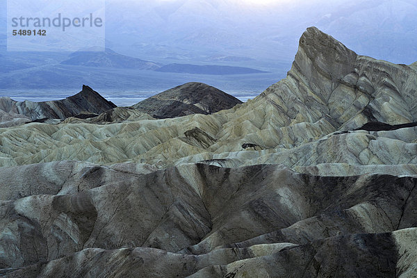 Blick von Zabriskie Point  Zabriske Point  auf durch Mineralien verfärbtes erodiertes Gestein des Manly Beacon  dahinter Panamint Range  Abenddämmerung  Death Valley Nationalpark  Mojave-Wüste  Kalifornien  Vereinigte Staaten von Amerika  USA