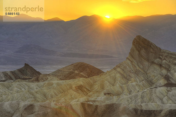 Blick von Zabriskie Point  Zabriske Point  auf durch Mineralien verfärbtes erodiertes Gestein des Manly Beacon  dahinter Panamint Range  Sonnenuntergang  Death Valley Nationalpark  Mojave-Wüste  Kalifornien  Vereinigte Staaten von Amerika  USA
