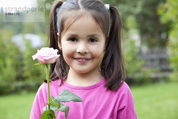 Mädchen hält Blume im Garten  lächelnd  Portrait