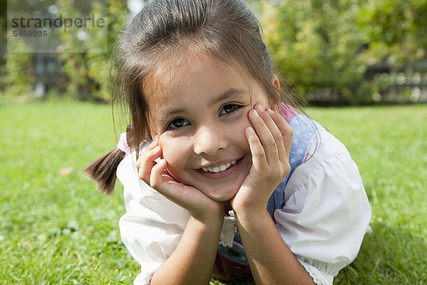 Mädchen in drindl liegend auf Gras im Garten  lächelnd  Portrait