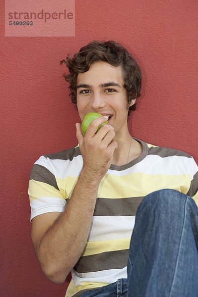 Junger Mann isst Apfel  lächelnd  Porträt