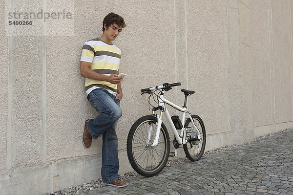 Junger Mann mit Telefon im Stehen auf dem Fahrrad
