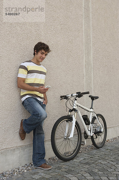 Junger Mann beim Telefonieren mit dem Fahrrad  lächelnd