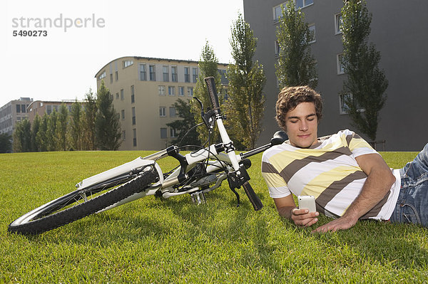 Junger Mann im Gras liegend mit Handy  lächelnd
