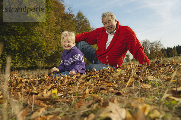 Deutschland  Bayern  Großvater und Enkelin sitzend Gras  lächelnd