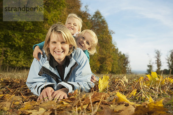 Deutschland  Bayern  Familie im Herbst auf Blättern liegend  lächelnd  Portrait