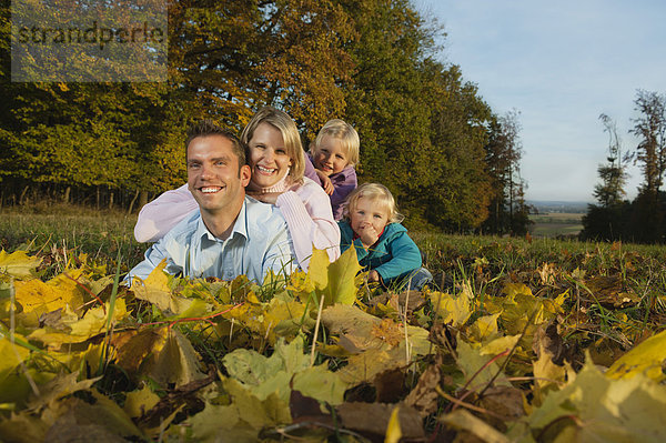 Deutschland  Bayern  Familie im Herbst auf Blättern liegend  Portrait  lächelnd