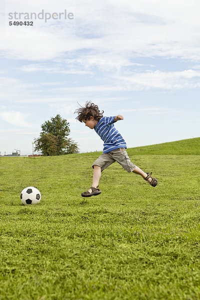 Junge spielt mit Fußball im Park.