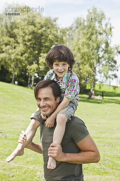 Deutschland  Bayern  Vater mit Sohn auf der Schulter im Park  lächelnd