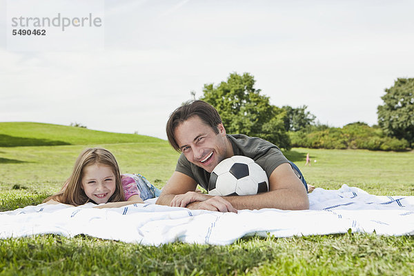 Deutschland  Bayern  Vater und Tochter im Gras liegend  lächelnd  Portrait