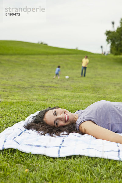Frau auf der Decke liegend  Vater und Sohn spielen Fußball im Park  lächelnd