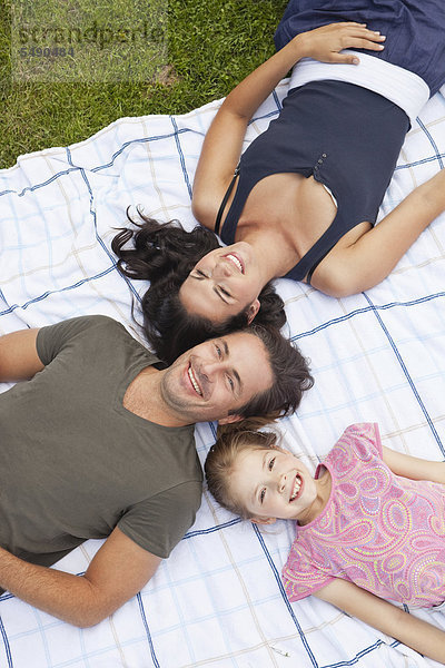 Deutschland  Bayern  Familie auf Decke im Park liegend  lächelnd