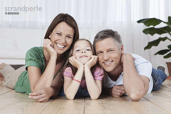 Deutschland  München  Eltern und Tochter auf dem Boden liegend  lächelnd  Portrait