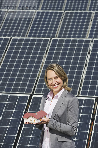 Frau mit Modellhaus gegen Sonnenkollektoren  lächelnd  Portrait